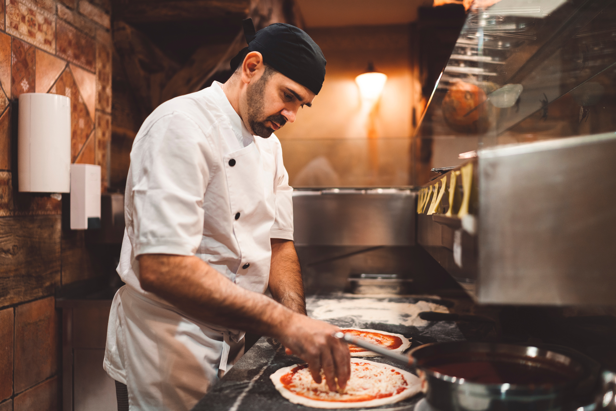 Pizza maker topping the pizza with mozzarella cheese